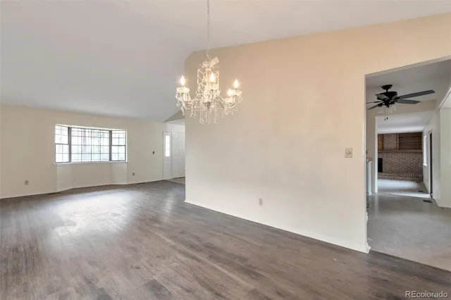 an empty room with wooden floor chandelier and windows