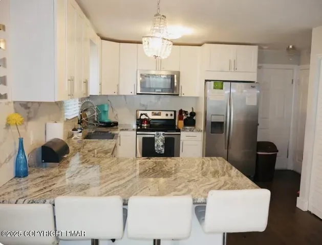 a kitchen with stainless steel appliances kitchen island granite countertop a refrigerator a sink a stove and chairs with wooden floor