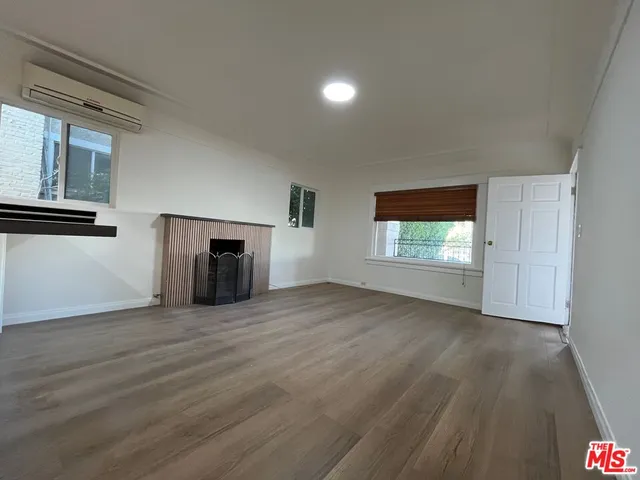 an empty room with wooden floor fireplace and windows