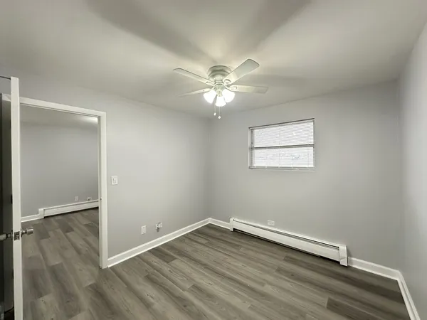 an empty room with wooden floor fan and windows