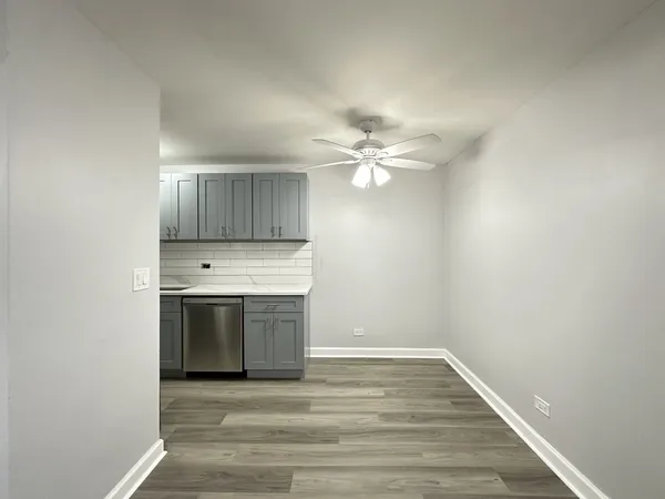 a view of an empty room with wooden floor and a kitchen