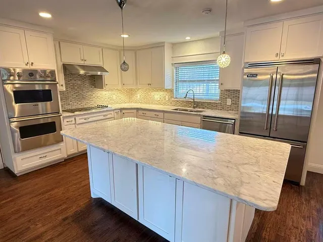 a large kitchen with granite countertop a large counter top stainless steel appliances and cabinets