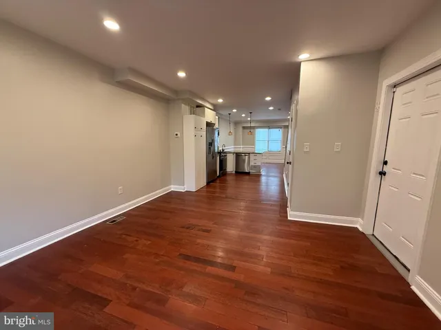an empty room with wooden floor and a kitchen