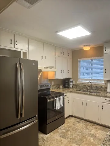 a kitchen with stainless steel appliances granite countertop a refrigerator a sink and white cabinets