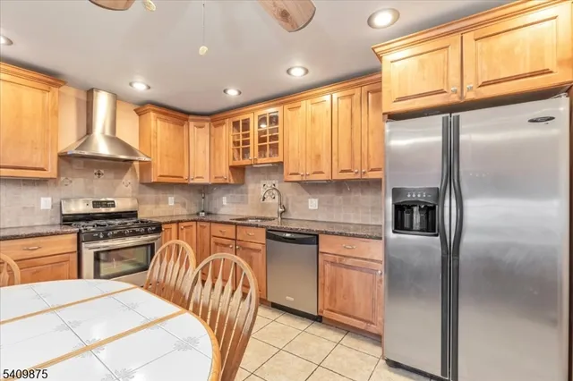 a kitchen with stainless steel appliances granite countertop a refrigerator a sink dishwasher a stove and white cabinets with wooden floor