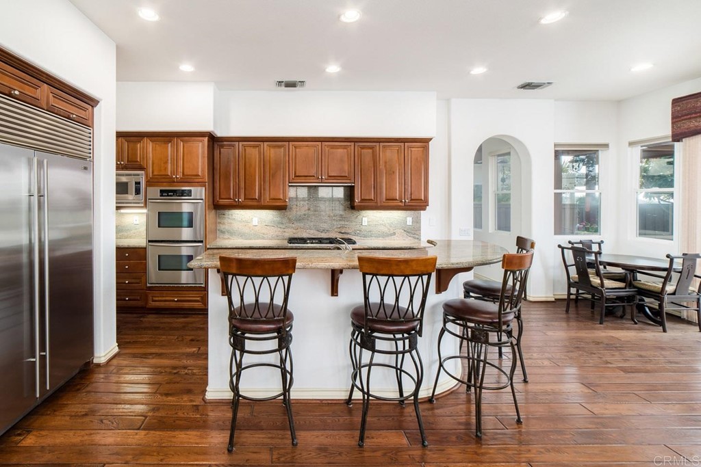 6237 Paseo Privado Carlsbad, CA 92009 - Photo 3 of 29 a kitchen with stainless steel appliances granite countertop a stove a refrigerator a kitchen island and chairs with wooden floor