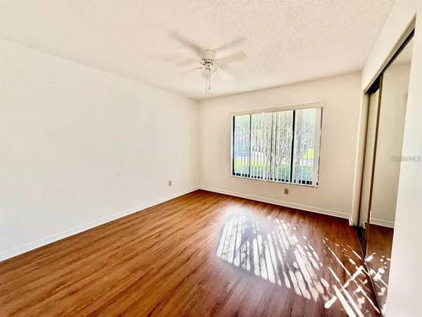 an empty room with wooden floor fan and windows