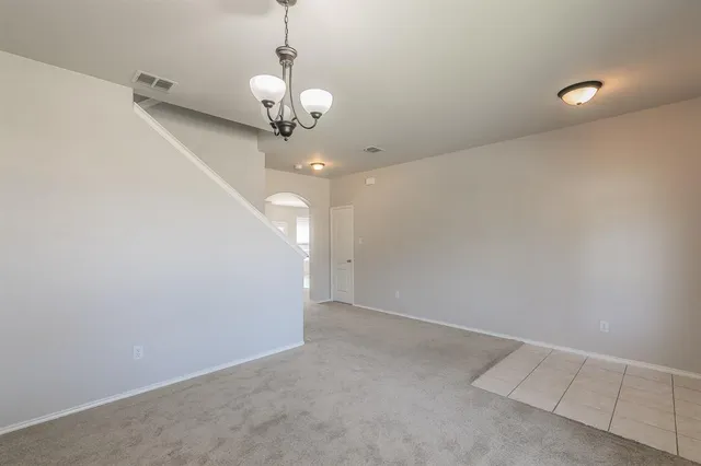 an empty room with a chandelier fan and view of a bathroom