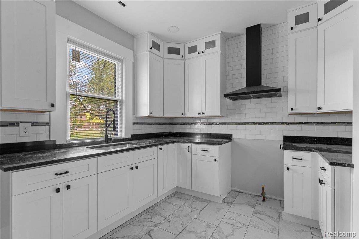 58 East Philadelphia Street Detroit, MI 48202 - Photo 12 of 24 Modern kitchen featuring white shaker cabinetry, dark countertops, a black wall-mounted range hood, a subway tile backsplash with accent band, and marble-look tile flooring