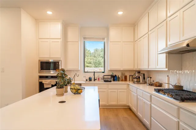 a kitchen with stainless steel appliances a sink a stove a refrigerator white cabinets and a window