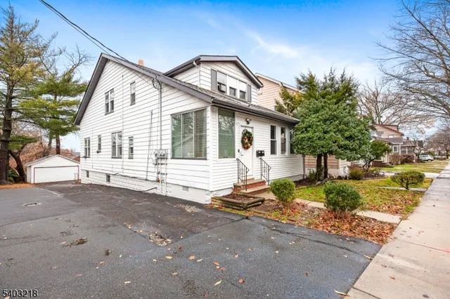 a view of a white house with a small yard and large trees