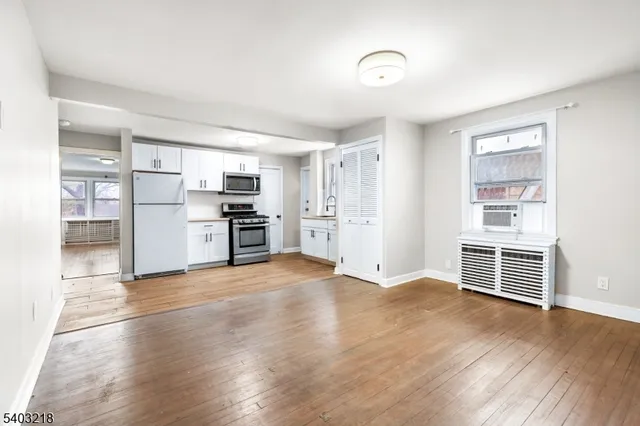 an empty room with wooden floor and a kitchen