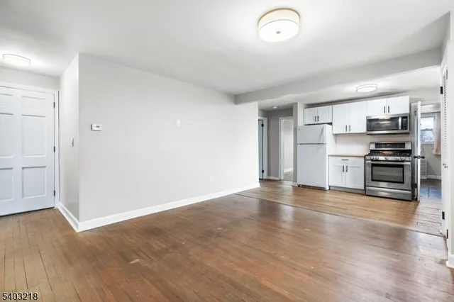 an empty room with wooden floor kitchen view and a window