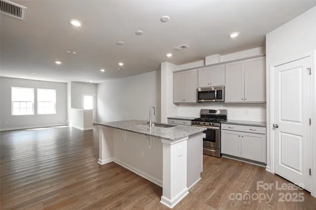 a kitchen with stainless steel appliances granite countertop a stove top oven a sink dishwasher and a refrigerator with wooden floor