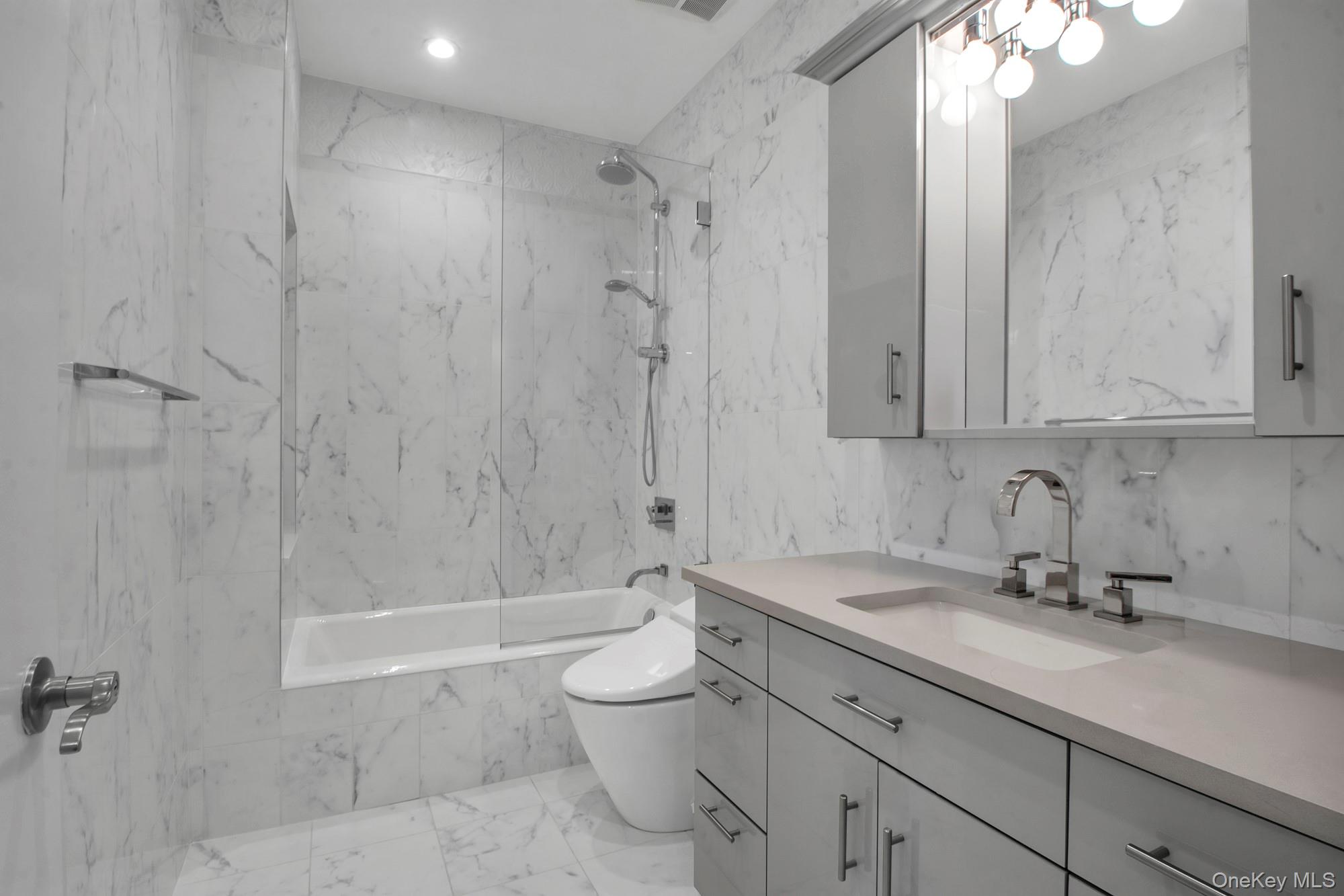102 Shore Road Queens, NY 11363 - Photo 15 of 22 Bathroom featuring stone wall, tile walls, vanity, a combined bath / shower with marble appearance, and light marble finish flooring