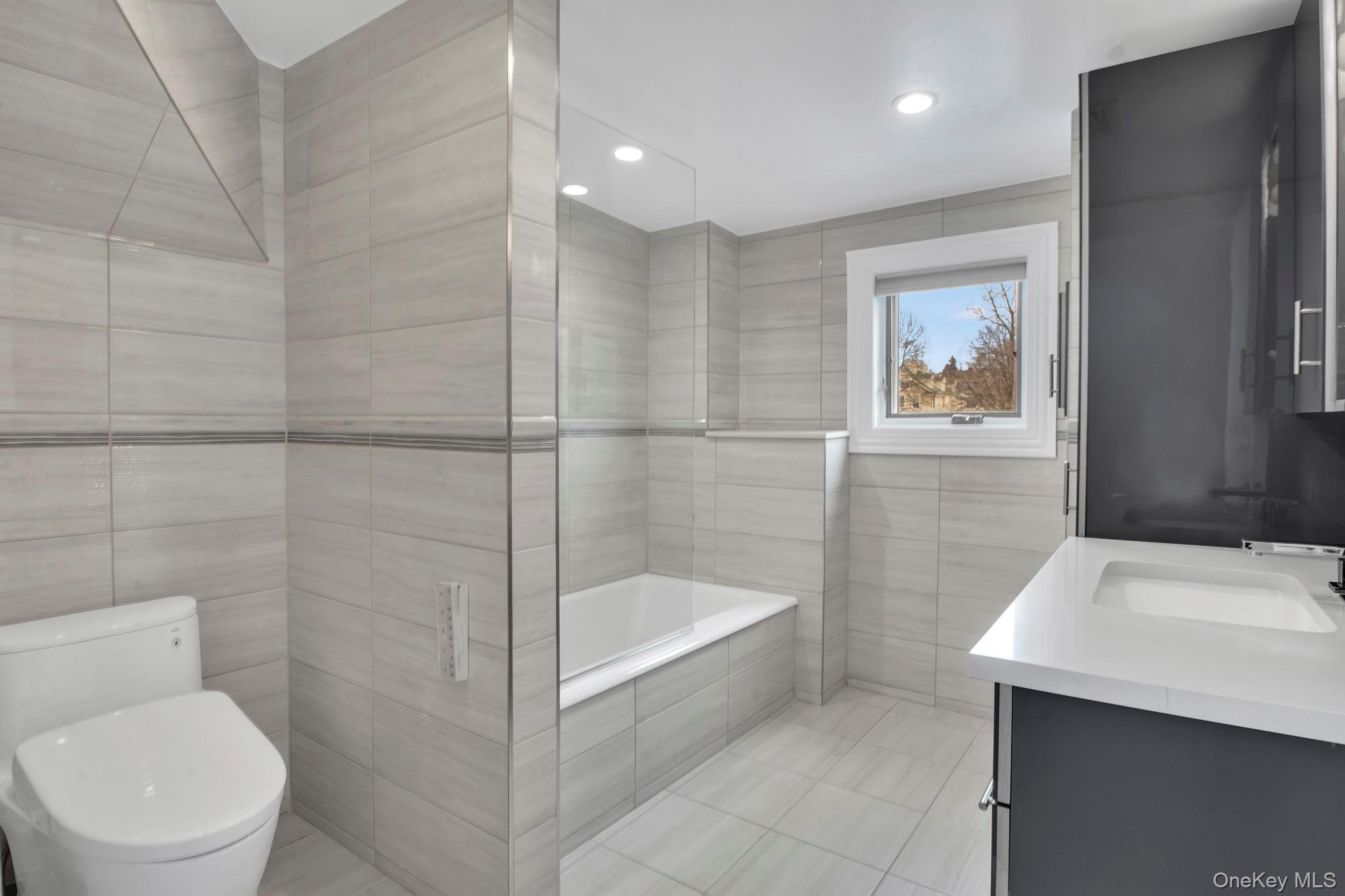 102 Shore Road Queens, NY 11363 - Photo 19 of 22 3rd floor windowed bathroom featuring tile walls, vanity, a bath, and recessed lighting