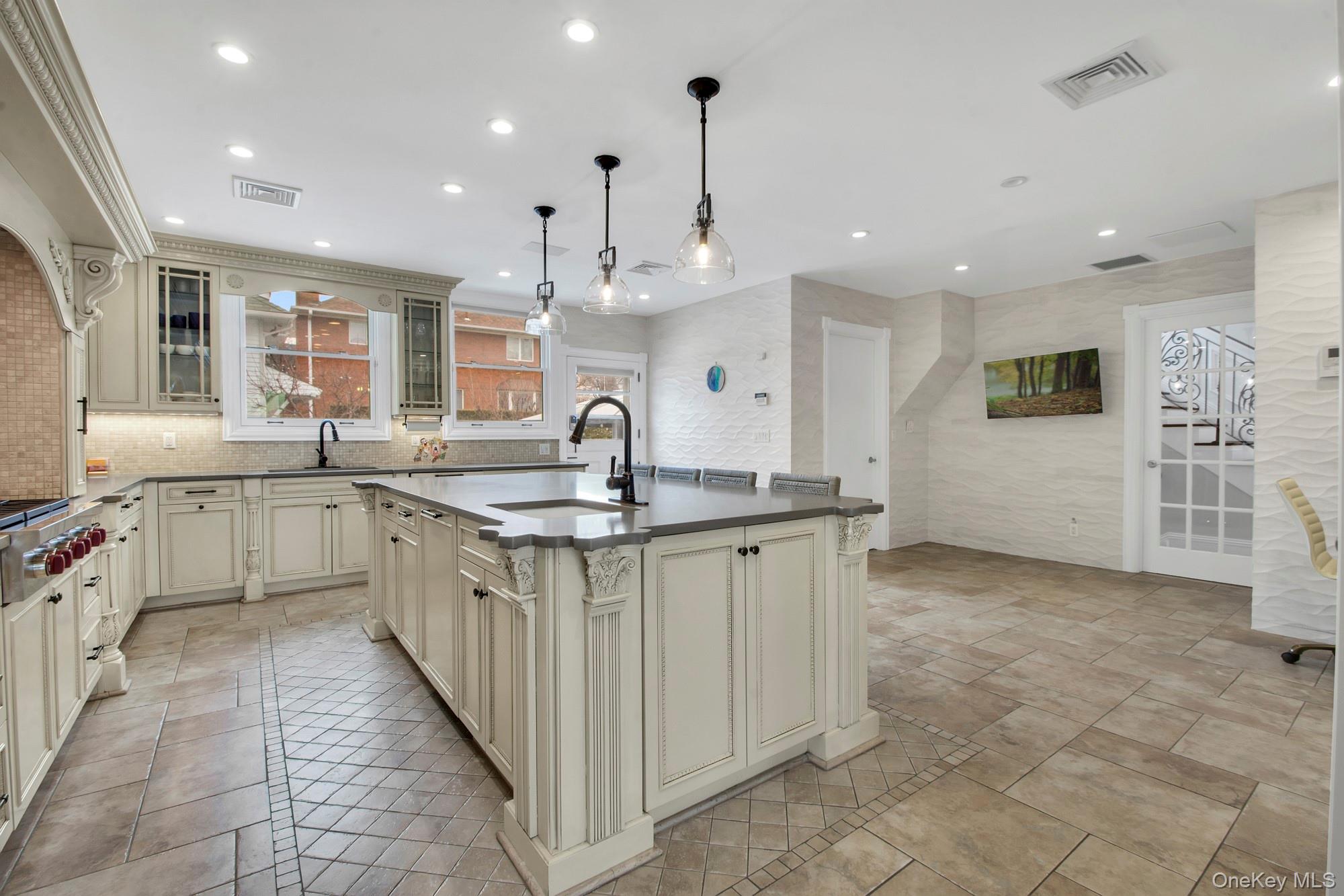 102 Shore Road Queens, NY 11363 - Photo 6 of 22 Eat-In-Kitchen with custom cabinetry, glass fronted cabinets, hanging light fixtures, a center island with sink, and light stone finish radiant floors, outdoor access