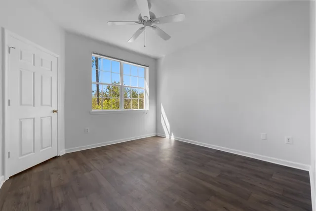 an empty room with wooden floor ceiling fan and windows