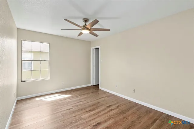 an empty room with wooden floor fan and windows