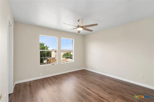 an empty room with wooden floor ceiling fan and windows