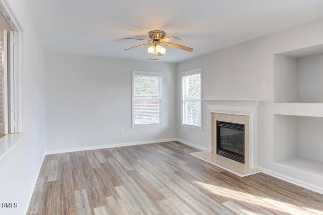 a view of an empty room with wooden floor fireplace and a window