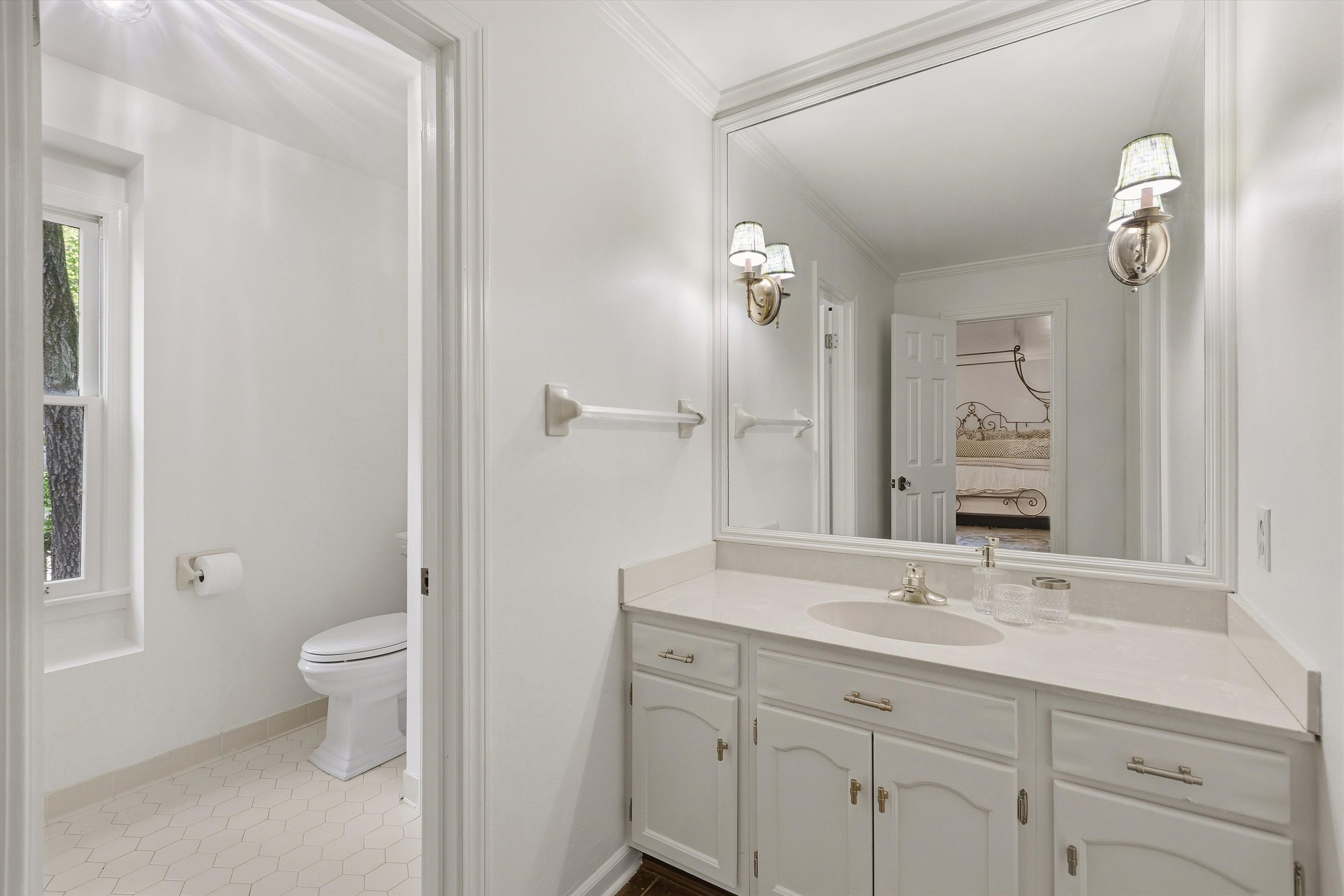 5828 Haymarket Road Memphis, TN 38120 - Photo 26 of 40 Bathroom featuring a single vanity with extensive countertop space and integrated sink, a large wall-mounted mirror, two sconce light fixtures, and a toilet in a separate alcove with a window