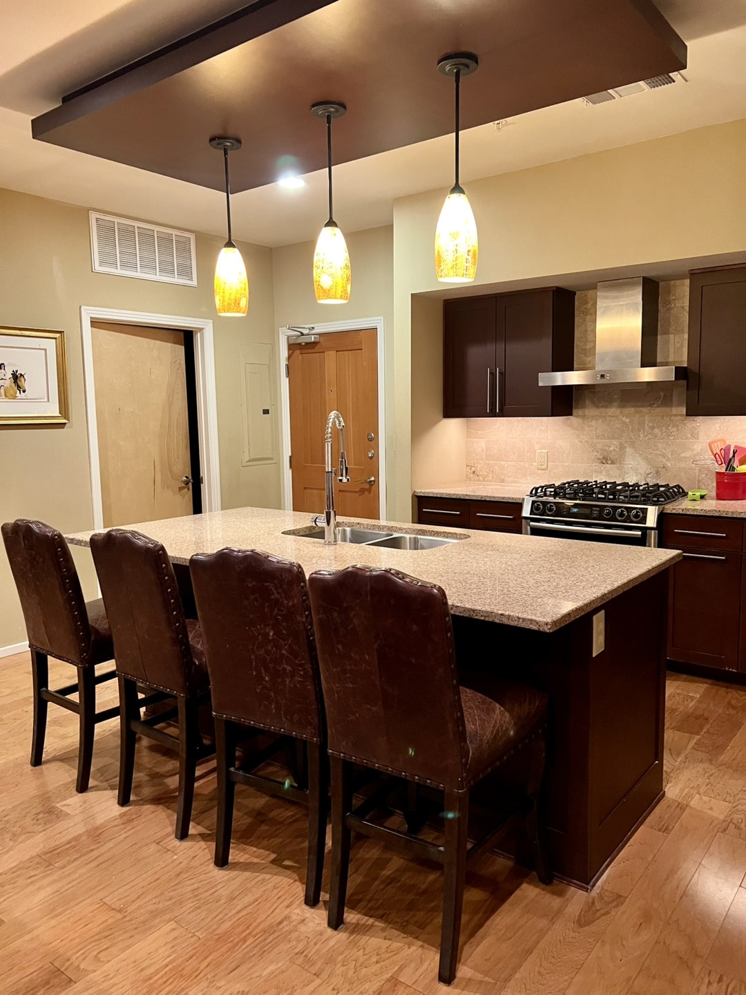 Kitchen featuring dark wood finish cabinetry, pendant lighting, tasteful backsplash, a kitchen bar, and stainless steel gas stove