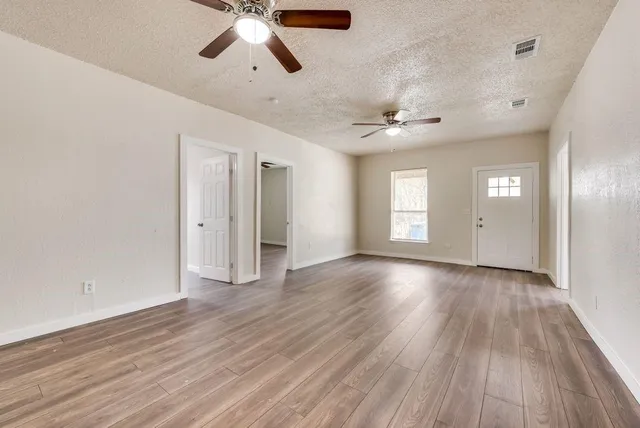 a view of an empty room with wooden floor and a ceiling fan