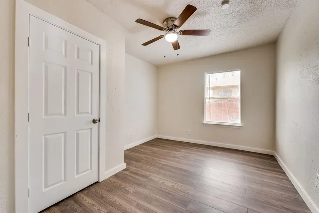 an empty room with wooden floor chandelier fan and windows