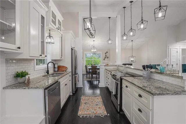 a kitchen with stainless steel appliances granite countertop a stove a sink dishwasher and white cabinets with wooden floor