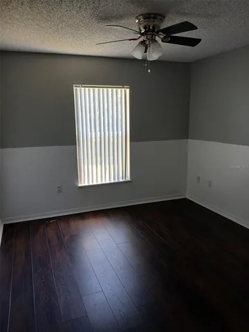 an empty room with wooden floor fan and windows