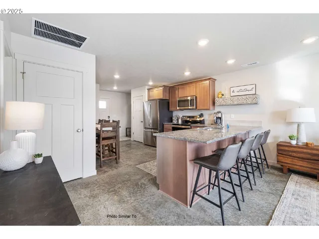 a kitchen with stainless steel appliances kitchen island granite countertop a refrigerator a stove a sink a dining table and chairs with wooden floor