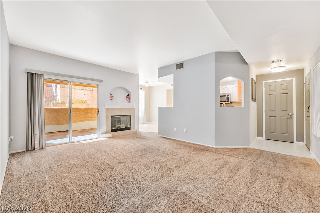 2050 West Warm Springs Road, Unit 2411 Henderson, NV 89014 - Photo 8 of 37 A spacious living room with plush carpet flooring and a cozy fireplace awaits, offering seamless access to an outdoor patio.