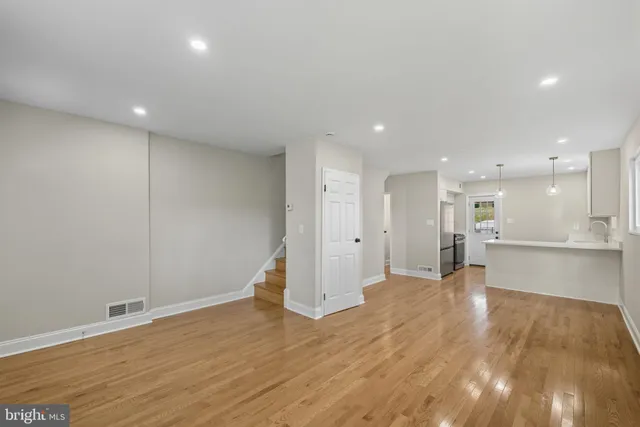 a view of an empty room with wooden floor and a kitchen