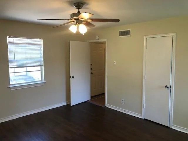an empty room with wooden floor chandelier fan and windows
