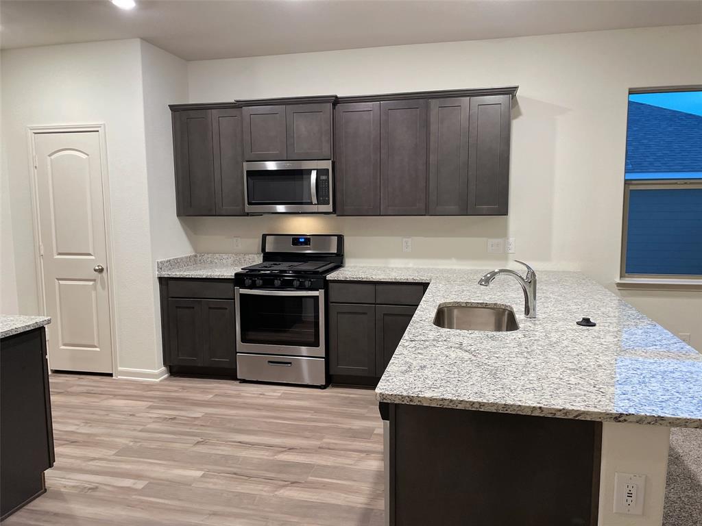 1819 Fergus Ponder, TX 76259 - Photo 6 of 8 a kitchen with granite countertop a stove top oven a sink dishwasher and wooden cabinets with wooden floor