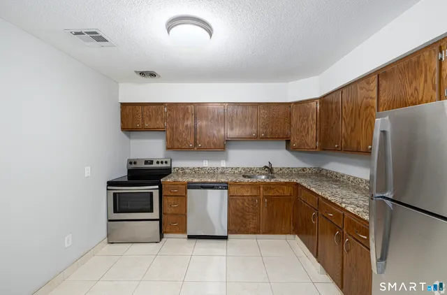 a kitchen with stainless steel appliances granite countertop a stove top oven a sink and dishwasher a refrigerator with wooden cabinets