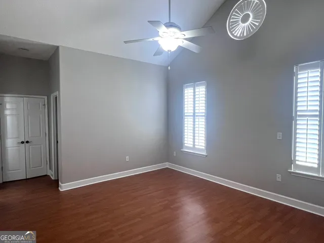 an empty room with wooden floor chandelier fan and windows