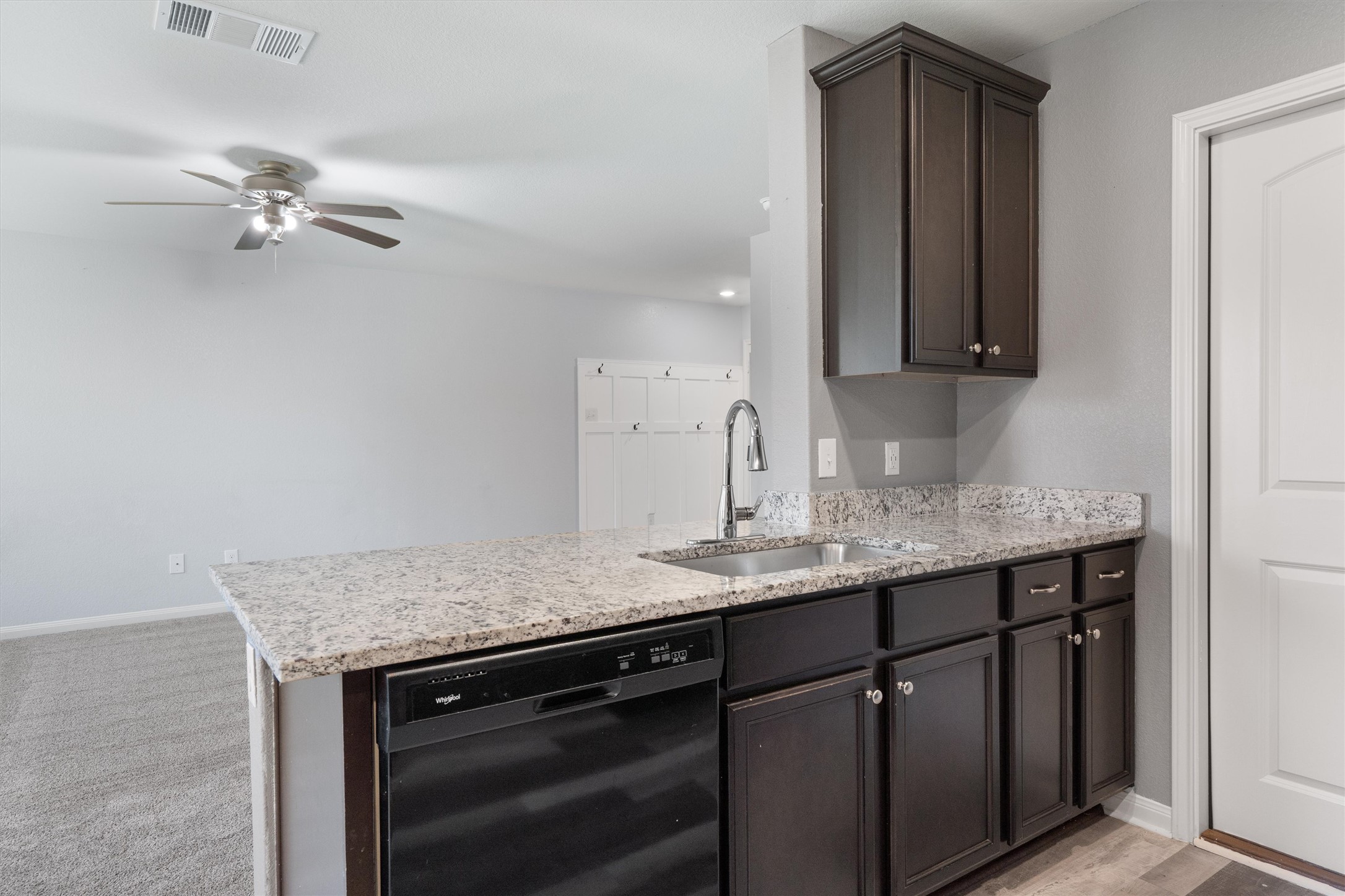 163 Niven Path, Unit 12K Jarrell, TX 76537 - Photo 8 of 39 Kitchen featuring black dishwasher, dark wood finish cabinetry, light stone countertops, and a breakfast bar.