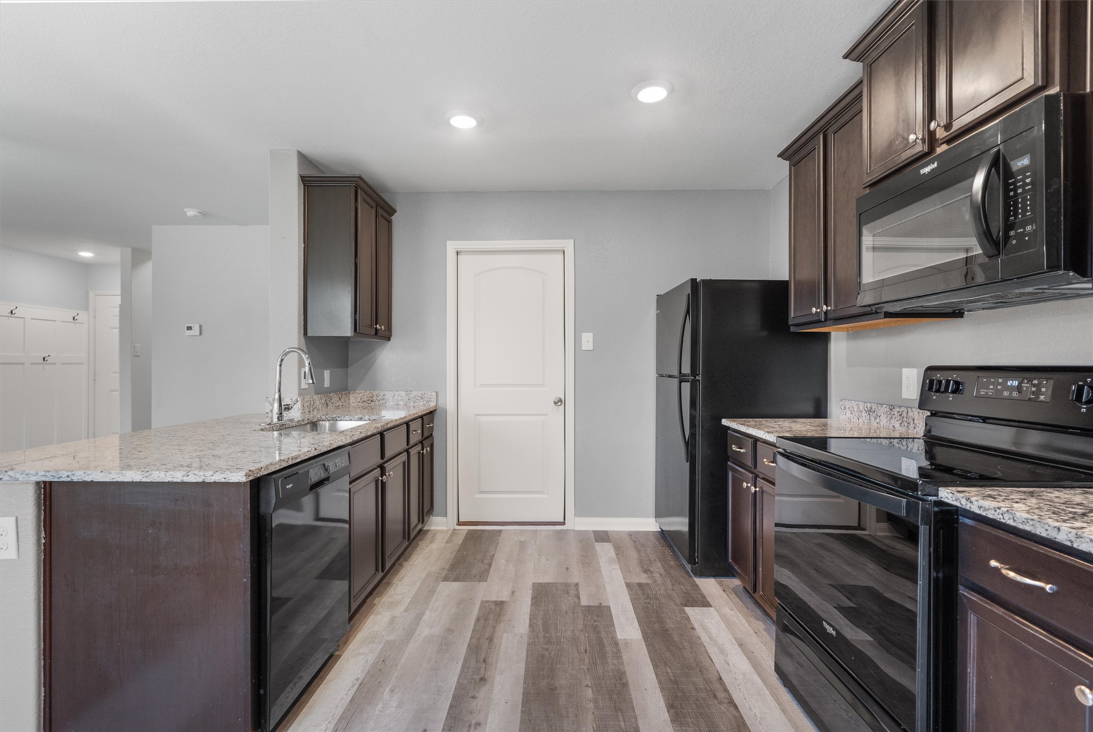 163 Niven Path, Unit 12K Jarrell, TX 76537 - Photo 9 of 39 Kitchen featuring dark wood finish cabinetry, black appliances, light stone counters, a peninsula, and recessed lighting.