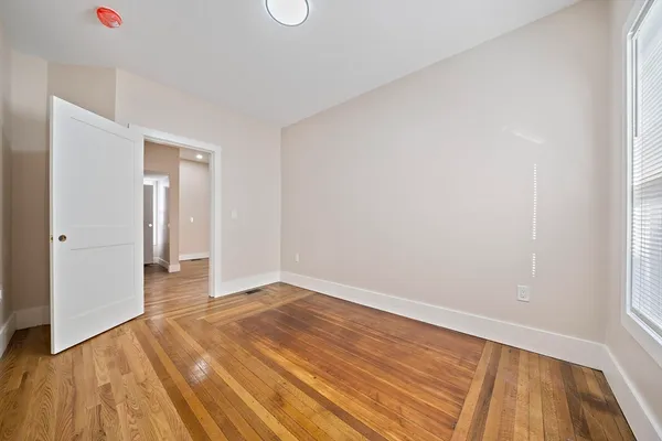 a view of an empty room with wooden floor and a window