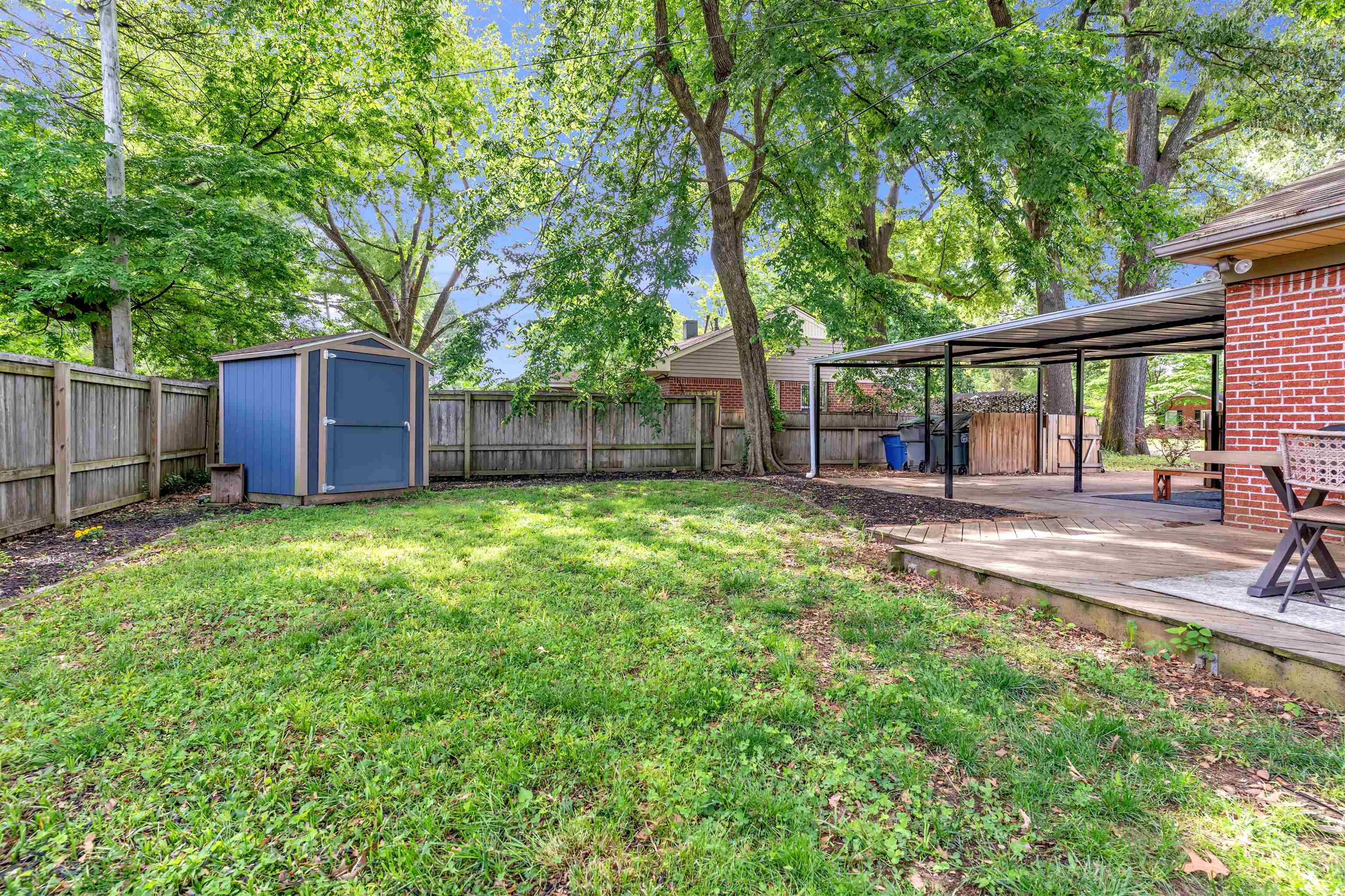 4564 Verne Road Memphis, TN 38117 - Photo 21 of 25 Expansive backyard featuring a manicured lawn, a blue storage shed, a wood fence perimeter, mature shade trees, and a covered patio area with a concrete surface