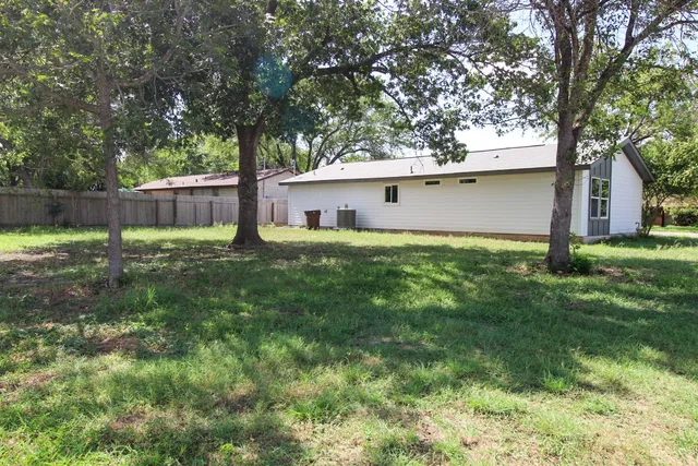 a backyard of a house with lawn chairs and a large tree
