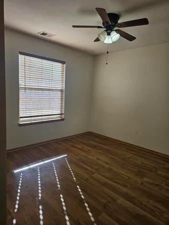 an empty room with wooden floor fan and windows