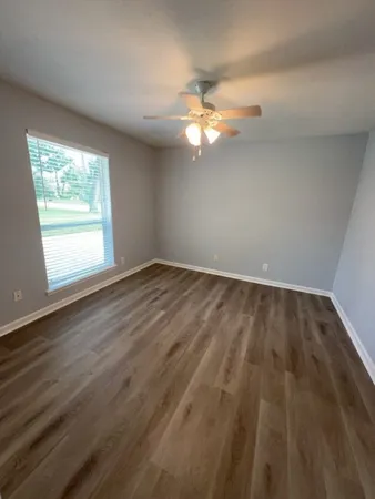 an empty room with wooden floor fan and window
