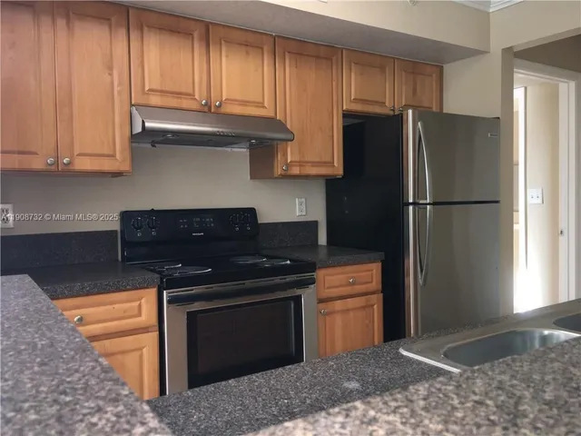 a kitchen with granite countertop wooden cabinets and a refrigerator