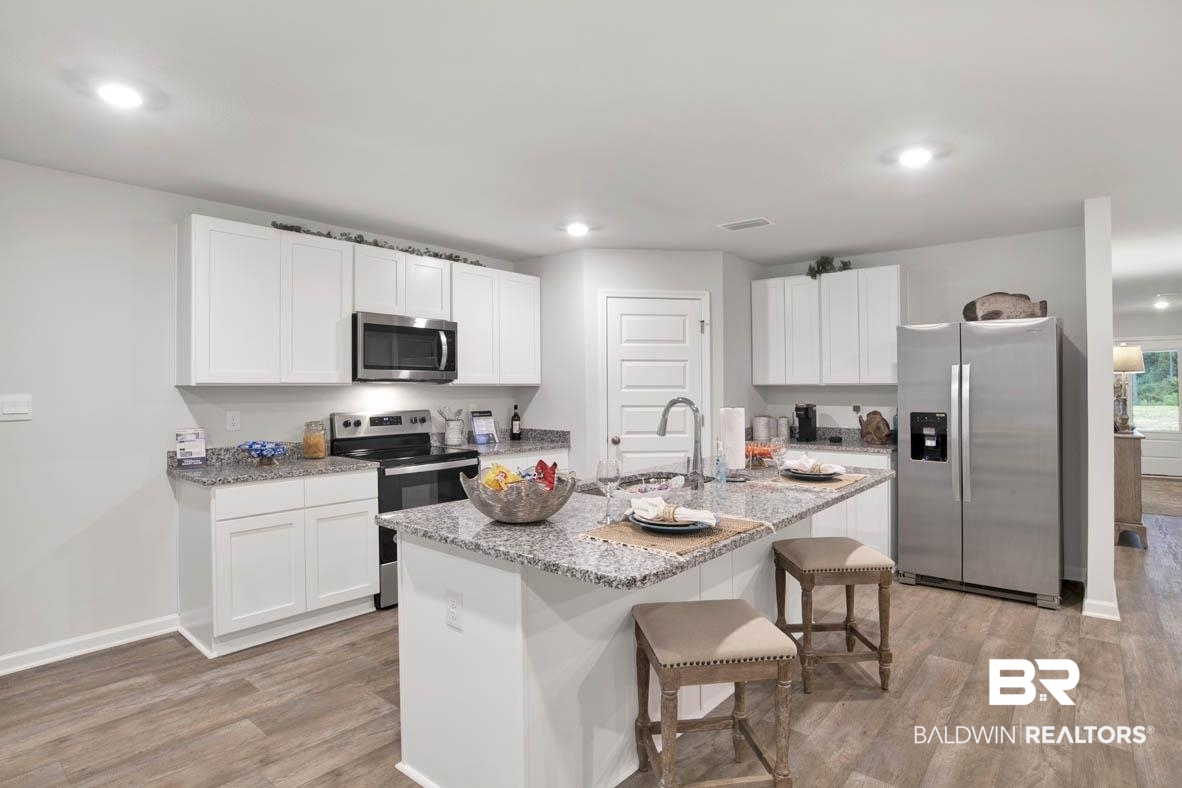 1235 Hayward Loop Foley, AL 36535 - Photo 12 of 26 Kitchen featuring light stone countertops, a center island with sink, light hardwood / wood-style floors, stainless steel appliances, and sink