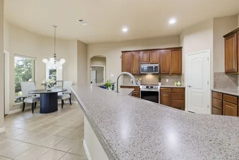 an empty room with a chandelier fan and kitchen view