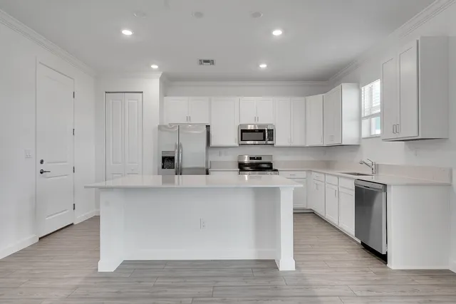 a kitchen with stainless steel appliances a sink a stove a refrigerator and white cabinets