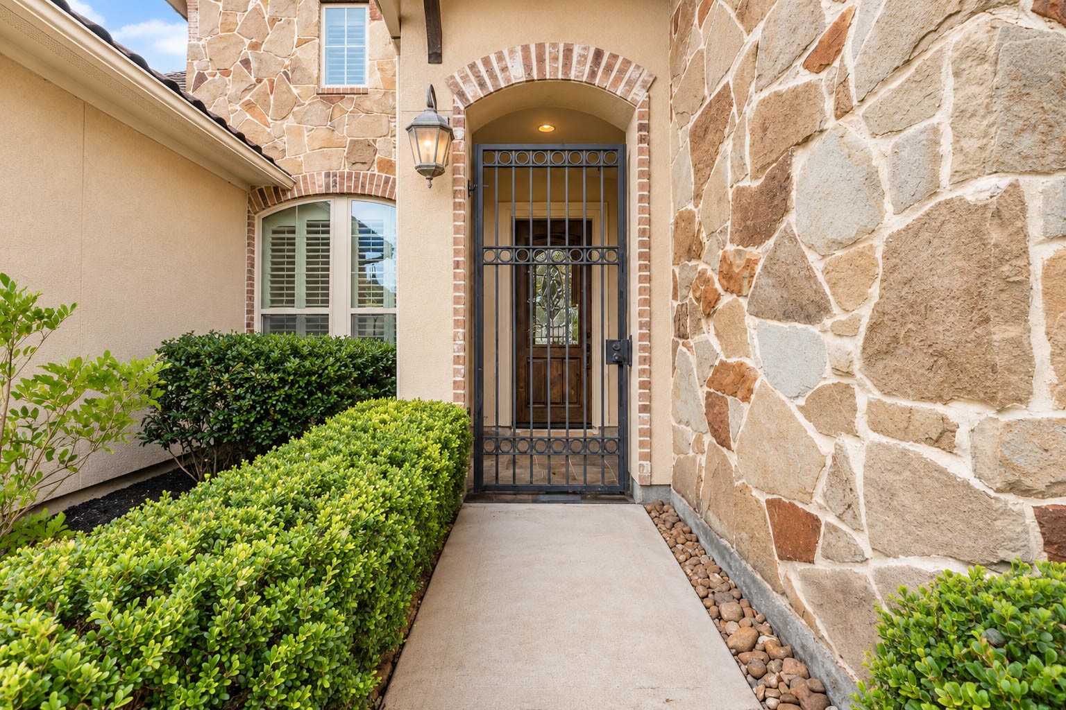 91 Lake View Loop Fulshear, TX 77441 - Photo 10 of 42 Follow the beautifully landscaped pathway to a gated entry that leads to the front door and porch. Take note of the lush greenery, gleaming windows, and striking stone and stucco exterior that welcome you home!